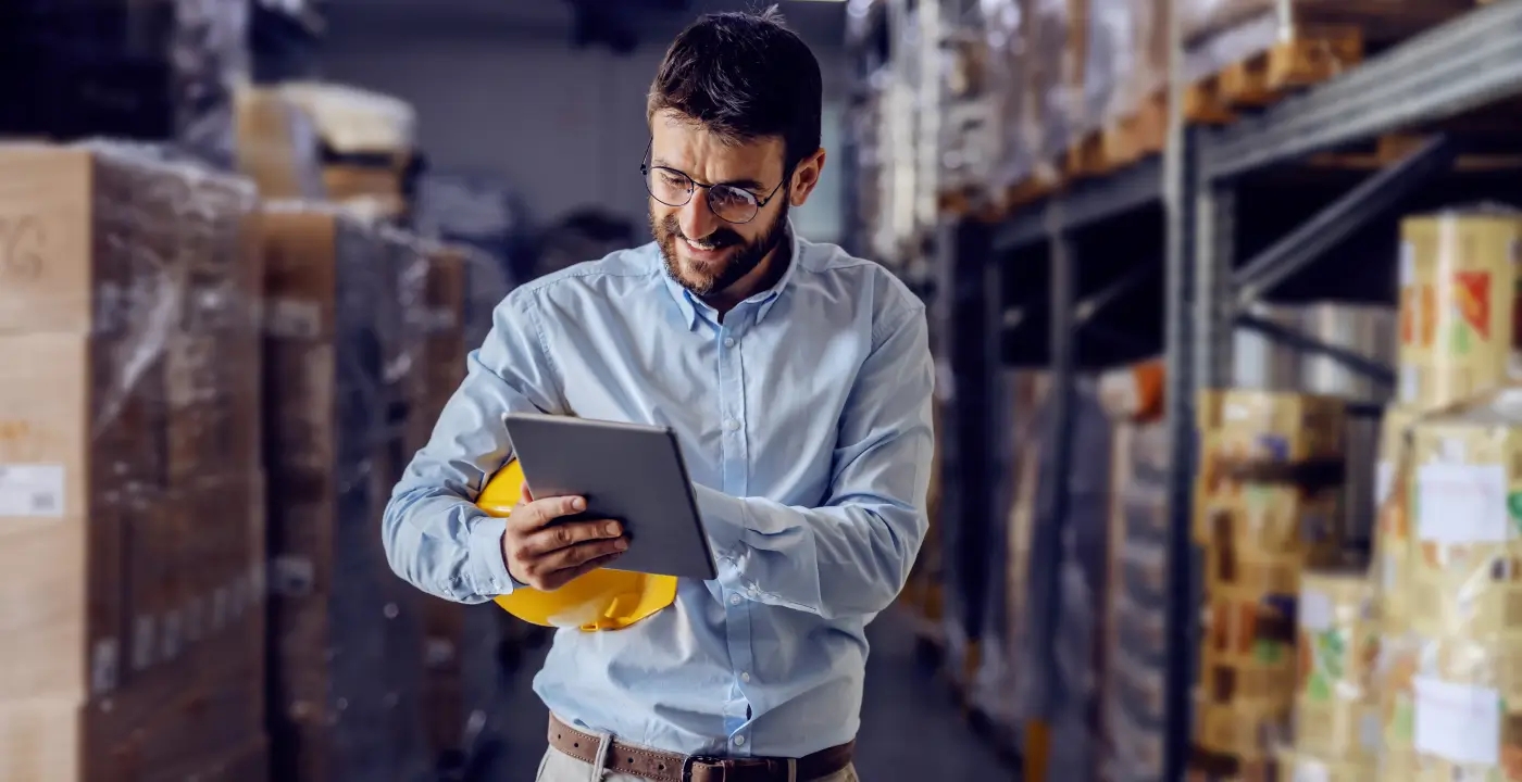 A man in a warehouse holding a tablet computer, ensuring reporting accuracy.