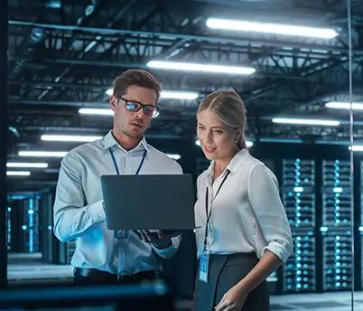 Two individuals in a server room, using a laptop for cloud computing management