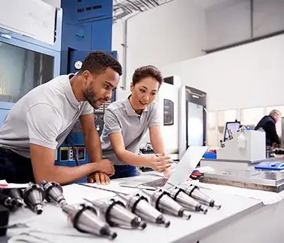 Image of two individuals using a laptop in a factory, symbolizing IT staff augmentation