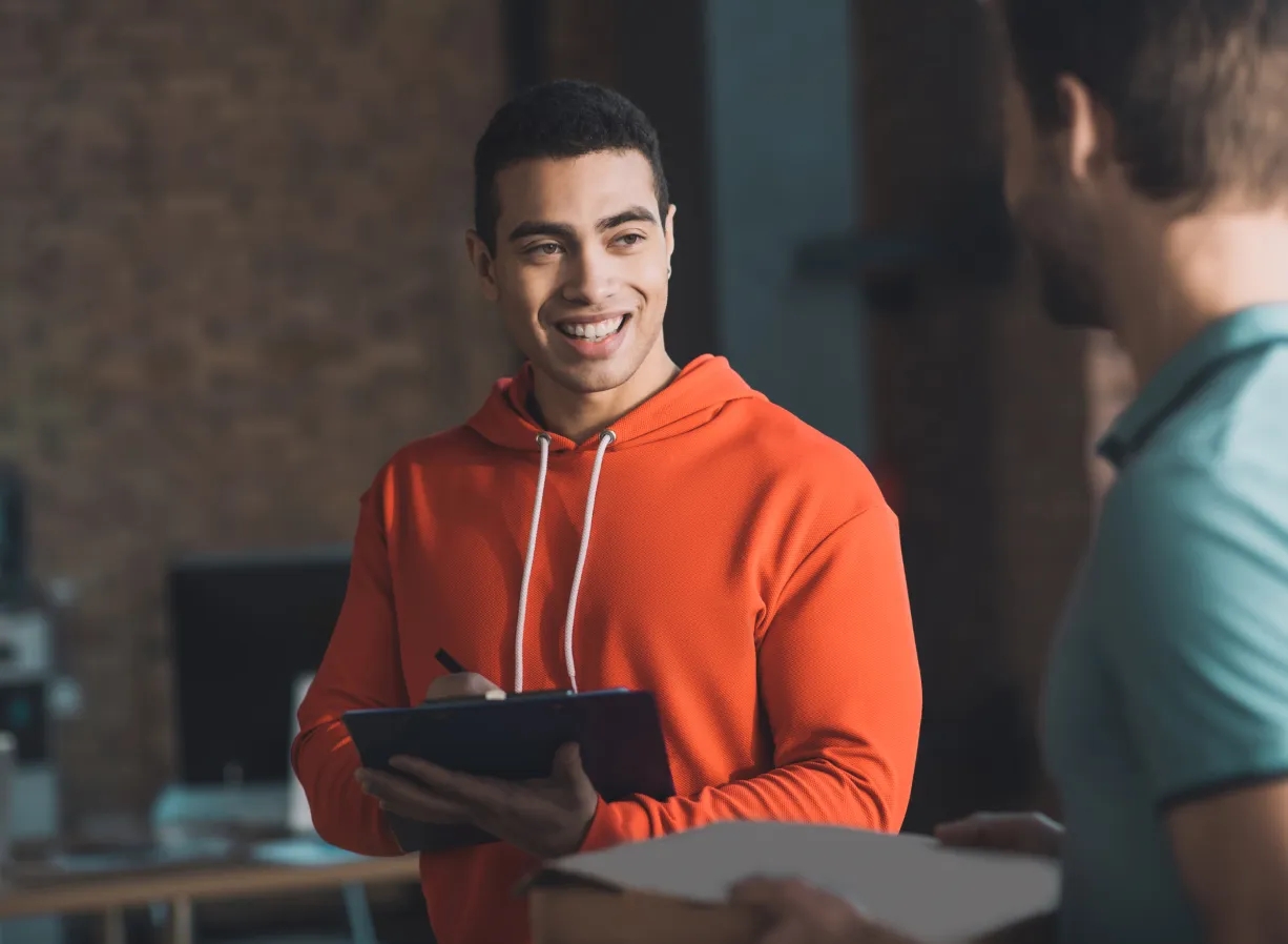 A man in an orange sweatshirt conversing with another man about cloud management internal IT support